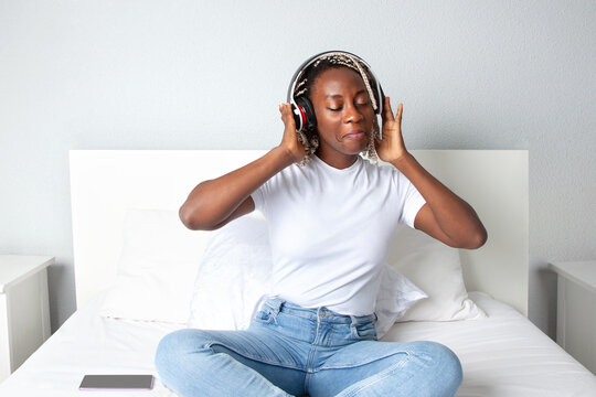 Mujer negra sonriente escuchando m&uacute;sica con auriculares en la habitaci&oacute;n de su casa. Lifestyle.