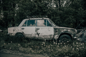 Old rusty abandoned car in the grass. LADA car. Shabby doors and car parts. Abandoned car in the forest. Mystical forest. The ghost of an old car.