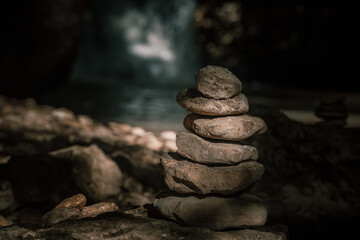 The figure of the stones on the background of the waterfall. The play of light and shadow. Small stones are lined up on top of each other. Stone tower. Light falls on the stones. A beautiful warm even
