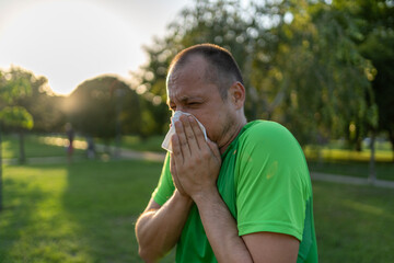 Allergic man blowing on wipe in a park on summer season