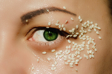 Open, green eye of a woman with white sesame seeds on the eyelid, around the eye. Expressive look.