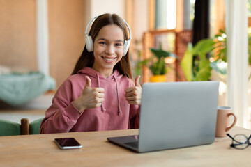 Like homeschooling. Portrait of positive teen girl studying with laptop from home, showing thumbs up