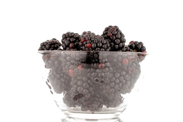 Several sweet blackberries in a glass bowl, close-up, isolated on a white background.