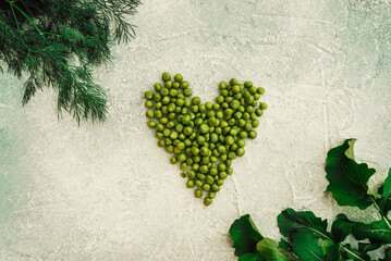 heart with fresh green peas, organic farm greens, dill and arugula on a gray concrete background