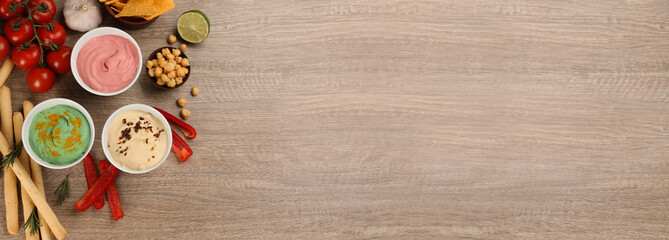 Different delicious hummuses on wooden table, flat lay with space for text. Banner design