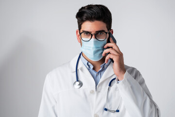 Studio portrait of male doctor wearing face mask and having a phone call while standing at isolated...