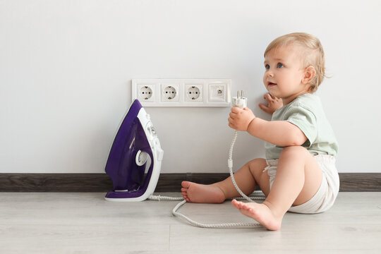 Cute Baby Playing With Electrical Socket And Iron Plug At Home. Dangerous Situation