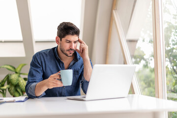 Thinking businessman sitting at desk and using laptop while working from home.