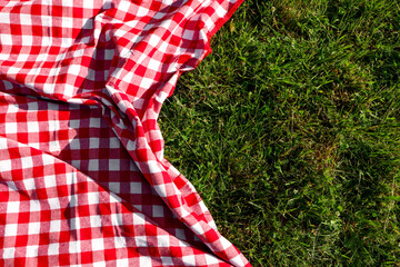 Checkered picnic tablecloth on fresh green grass, top view. Space for text