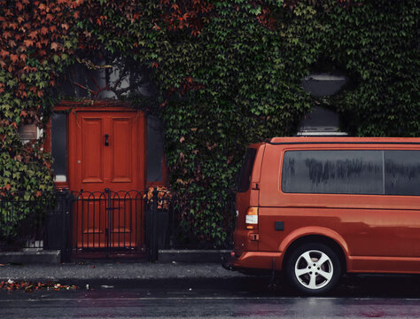 Red minivan parks in front of a house with a red door