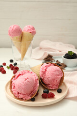 Delicious pink ice cream in wafer cones with berries on white wooden table