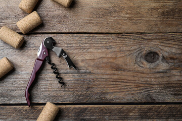 Corkscrew and wine corks on wooden table, flat lay. Space for text