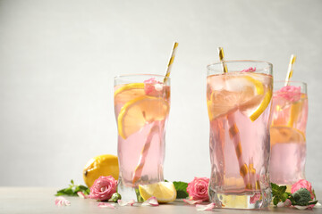 Delicious refreshing drink with rose flowers and lemon slices on light grey table