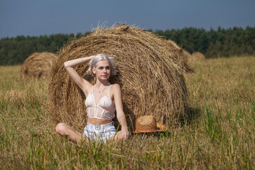 Naklejka na ściany i meble Young beautiful blonde girl in a straw hat posing in the hayloft