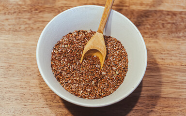 Selective focus on linseed or flax seed and a spoon in a white bowl on wooden background. Top view., close up and filtered photo. Healthy food concept. Copy for text. Noise effect and grainy texture. 