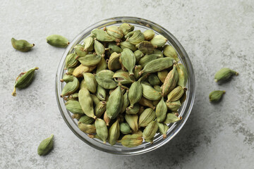 Glass bowl with dry cardamom pods on light grey table, top view