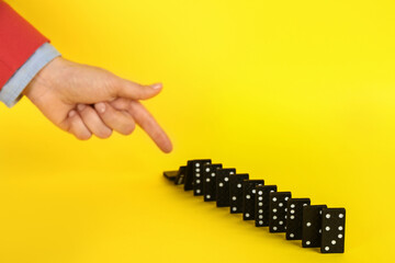 Woman causing chain reaction by pushing domino tile on yellow background, closeup