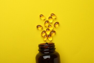 Overturned bottle with dietary supplement capsules on yellow background, flat lay