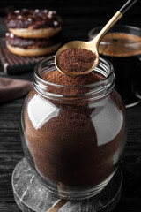 Spoon of instant coffee over jar on black wooden table