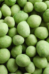 Tasty wasabi coated peanuts as background, top view