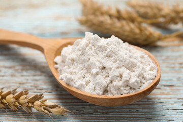 Spoon of wheat flour on light wooden table, closeup