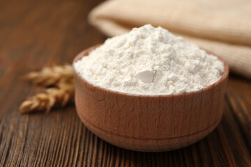 Bowl of organic wheat flour on wooden table, closeup