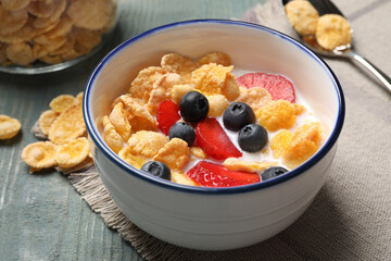 Delicious crispy cornflakes with milk and fresh berries on light blue wooden table, closeup