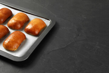 Delicious baked pirozhki on black table, space for text
