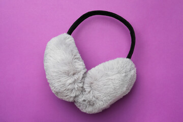 Stylish winter earmuffs on purple background, top view