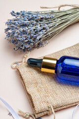 Blue Glass bottle with cosmetic oil or serum and lavender flowers on a beige background. Concept of lavender fragrance, skin care. Mockup
