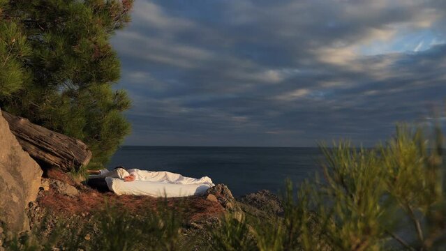 the girl Wakes Up in a stunning place of nature overlooking the ocean, stretches and looks around, static handheld shot