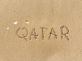 on the beach is carved with letters in the smooth sand the writing Qatar