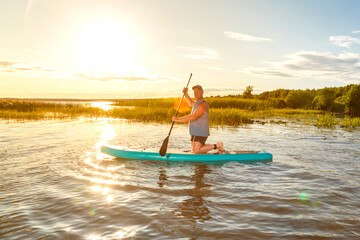 a man in shorts sits on a sup board at sunset in the water.