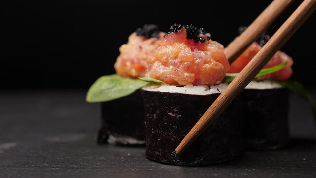 Take one sushi roll from black slate board using chopsticks, Closeup
