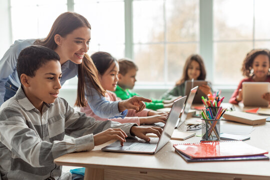 Teacher Teaching Diverse School Kids Using Laptop In Classroom