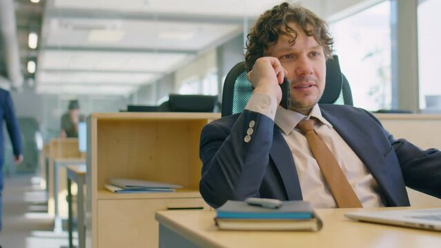 Businessman in formal suit speaking on mobile phone and then ending call while working at desk in office