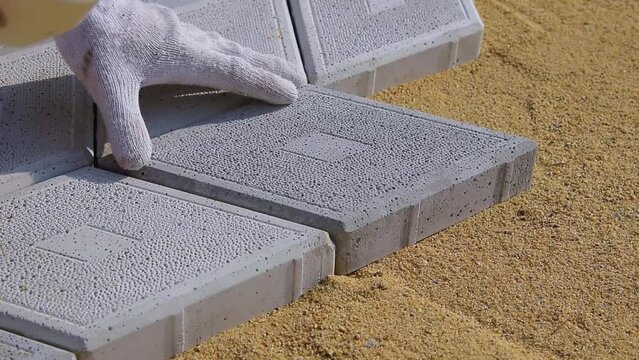 man lays paving slabs on the sand using a rubber hammer
