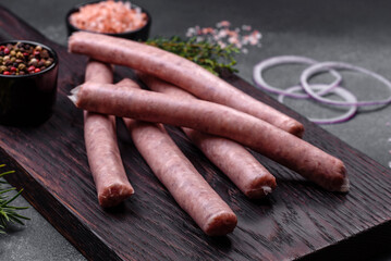 Raw sausages with spices on a wooden cutting board on a stone background with copy space for your text