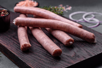 Raw sausages with spices on a wooden cutting board on a stone background with copy space for your text