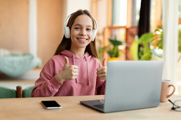 Best choice. Happy teenage girl with wireless headphones showing thumbs up to camera, enjoying...