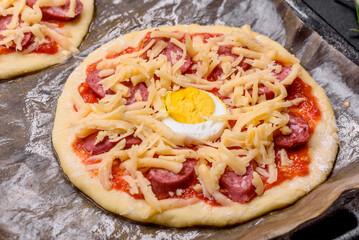 Homemade pizza with sausages, tomatoes, cheese, spices and herbs on a wooden cutting board