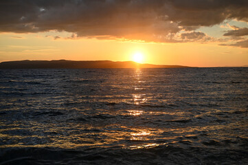 Tropical sunset with dramatic sky with clouds. Sun going down in orange sky over horizon. Silhouette of a island. Soft waves on the water.