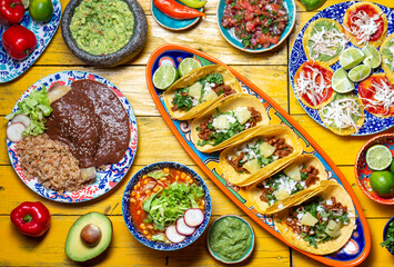 Mexican festive food for independence day independencia - chiles en nogada, tacos al pastor, chalupas pozole, tamales, chicken with mole poblano sauce. Yellow background.