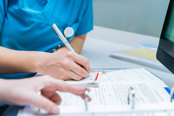 two nurses share patient information by writing it on the patient file, sharing paperwork and...