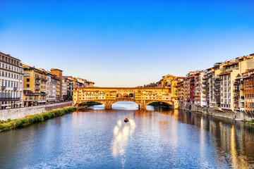 Obraz premium Golden Sunset over Ponte Vecchio Bridge with Traditional Boat on the Arno River