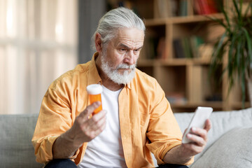 Concentrated senior man holding medicine and smartphone - Powered by Adobe