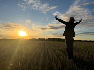Fototapeta kobieta z rozpostartymi rękoma na tle zachodzącego słońca obraz