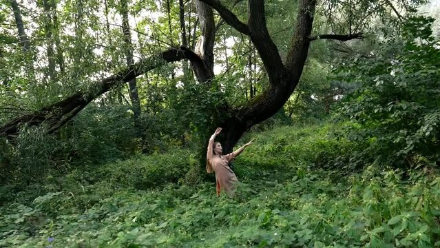 An elegant caucasian girl with a painted body performs an ecstatic dance improvisation in a lush tropical forest near. A young girl enjoys nature, relaxes with freedom and dances in the forest.