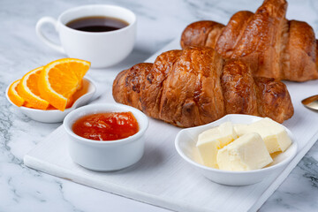 Fresh sweet croissants with butter and apricot jam for breakfast. Continental breakfast on a white concrete table