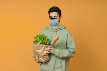 a man in a protective mask with a paper bag of products in his hands, colored background